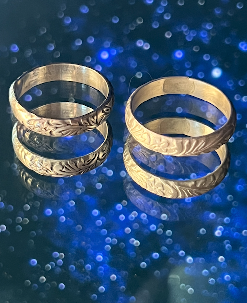 Two silver rings with engraved leaf patterns, stacked on a reflective dark surface with a starry night in the background.